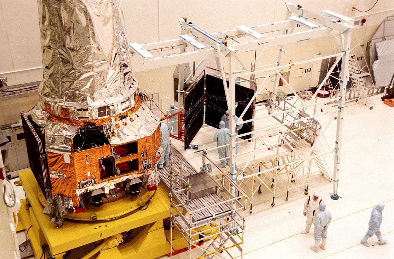 In the Vertical Processing Facility, TRW workers continue checking the deployment of the solar panel array (right) after attaching it to the Chandra X-ray Observatory (left). Formerly called the Advan