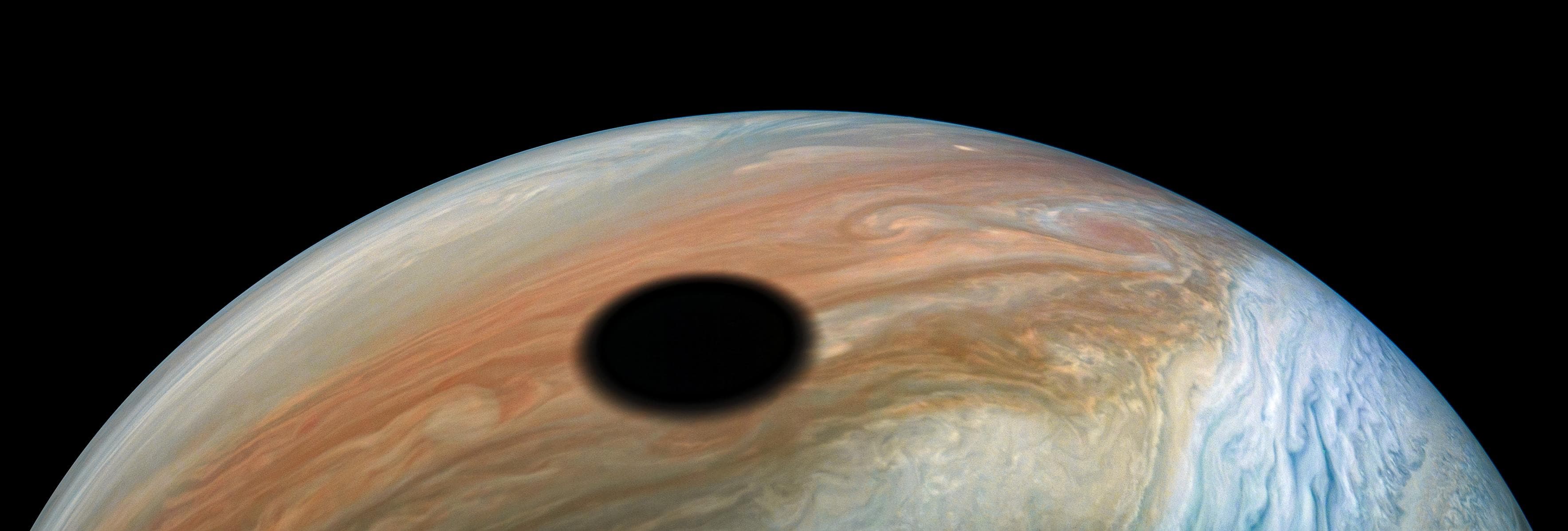 Jupiter's volcanically active moon Io casts its shadow on the planet in this dramatic image from NASA's Juno spacecraft. As with solar eclipses on the Earth, within the dark circle racing across Jupit