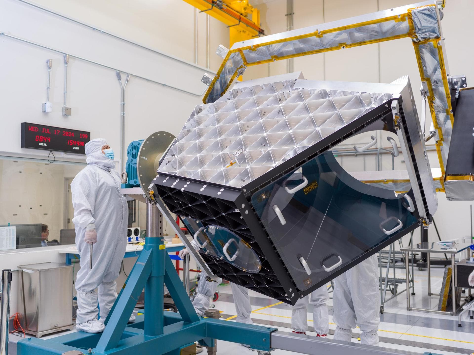 A technician operates articulating equipment to rotate the Near-Earth Object Surveyor (NEO Surveyor) mission's aluminum optical bench – part of the spacecraft's telescope – in a clean room at NASA's J