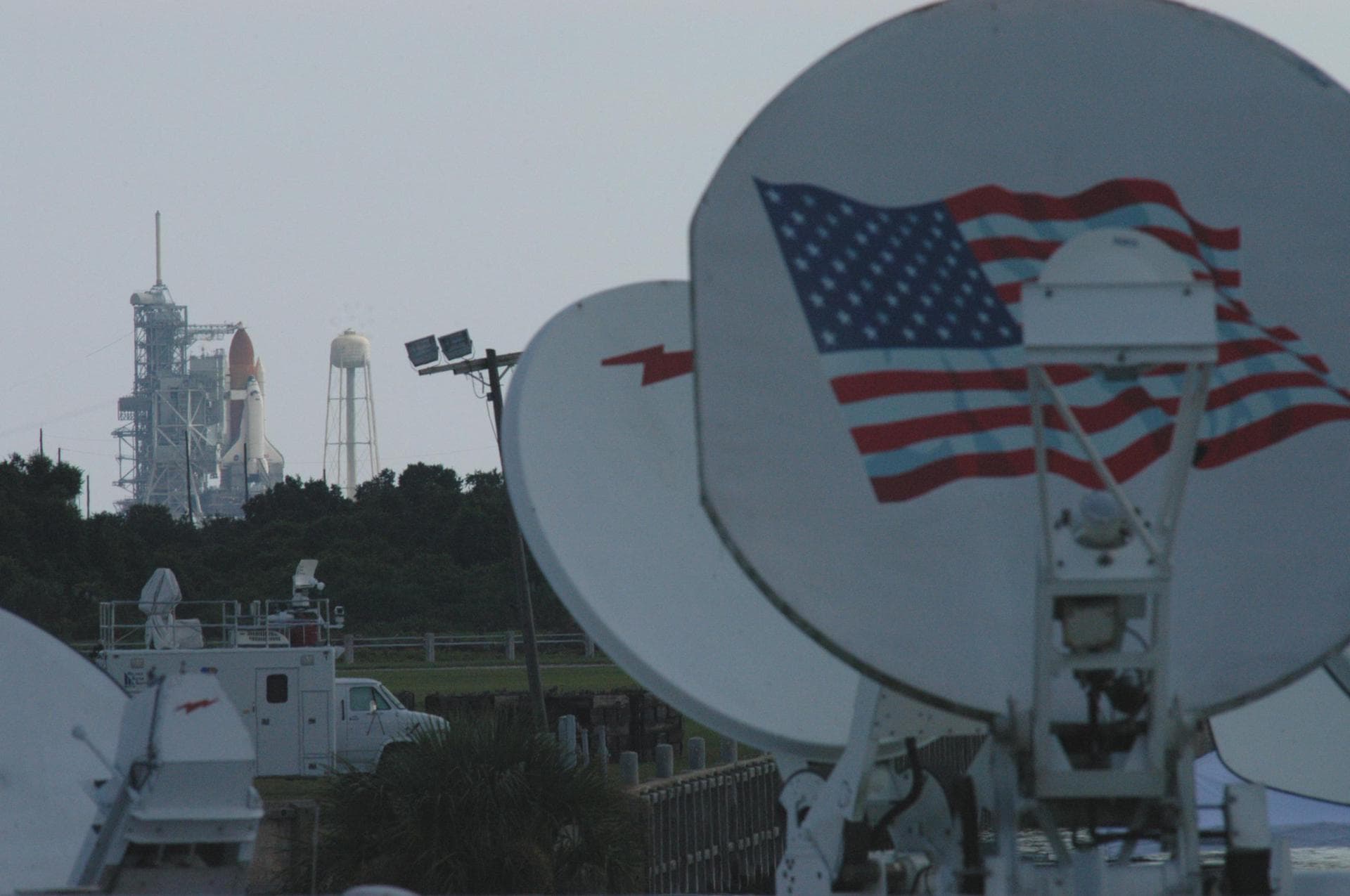 KENNEDY SPACE CENTER, FLA. - Satellite trucks are lined up at the NASA News Center to capture the launch of Space Shuttle Discovery from Launch Pad 39B (background) on the historic Return to Flight