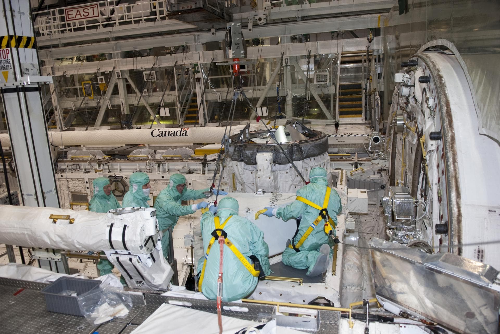 CAPE CANAVERAL, Fla. – In Orbiter Processing Facility-1 at NASA's Kennedy Space Center in Florida, workers dressed in clean room attire, known as bunny suits, guide the tool stowage assembly into posi