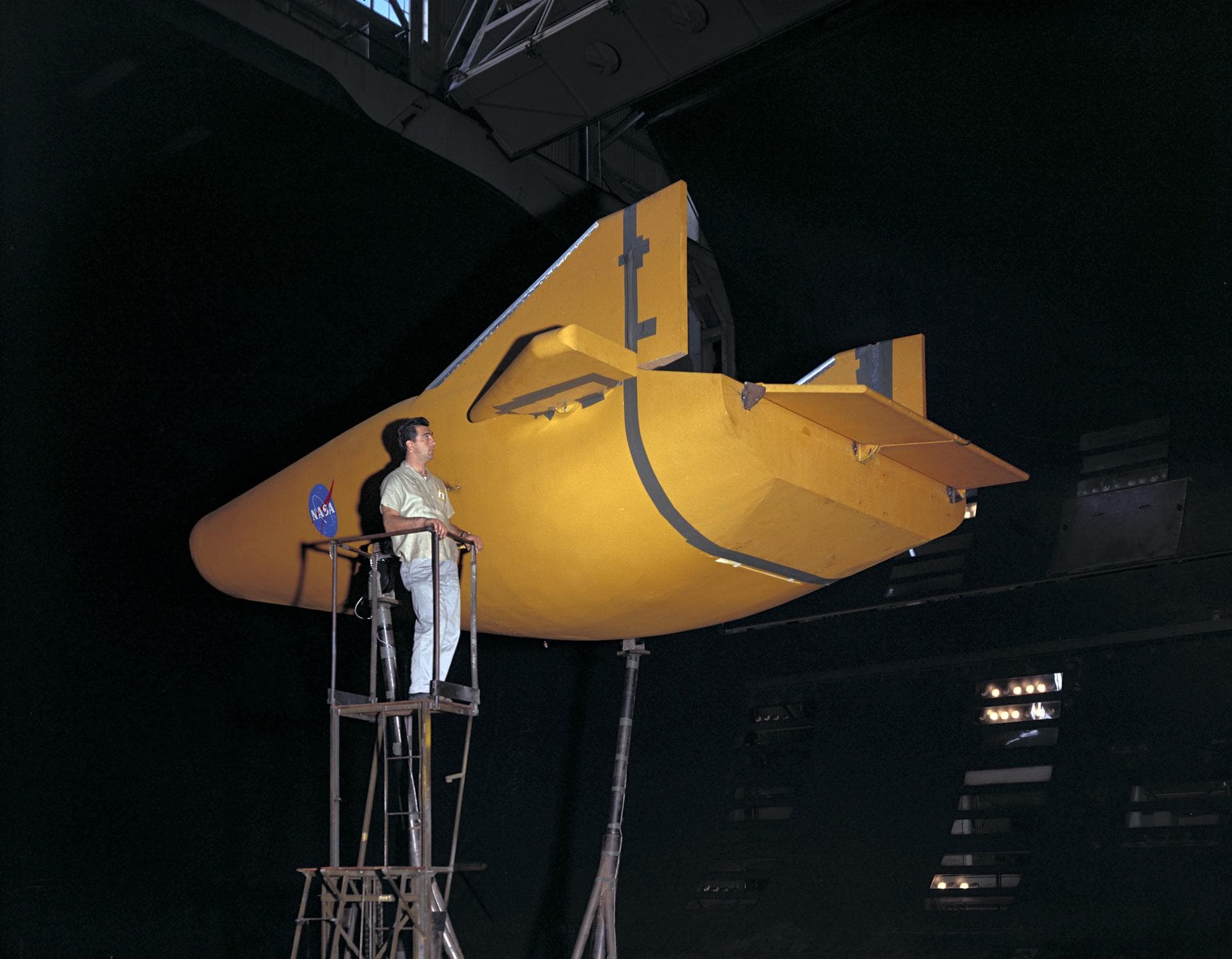 M-2 lifting body wind tunnel model with wind tunnel mechanic Chuck Greco. Model mounted on special support designed for lifting body models. Flaps and elevons visible.