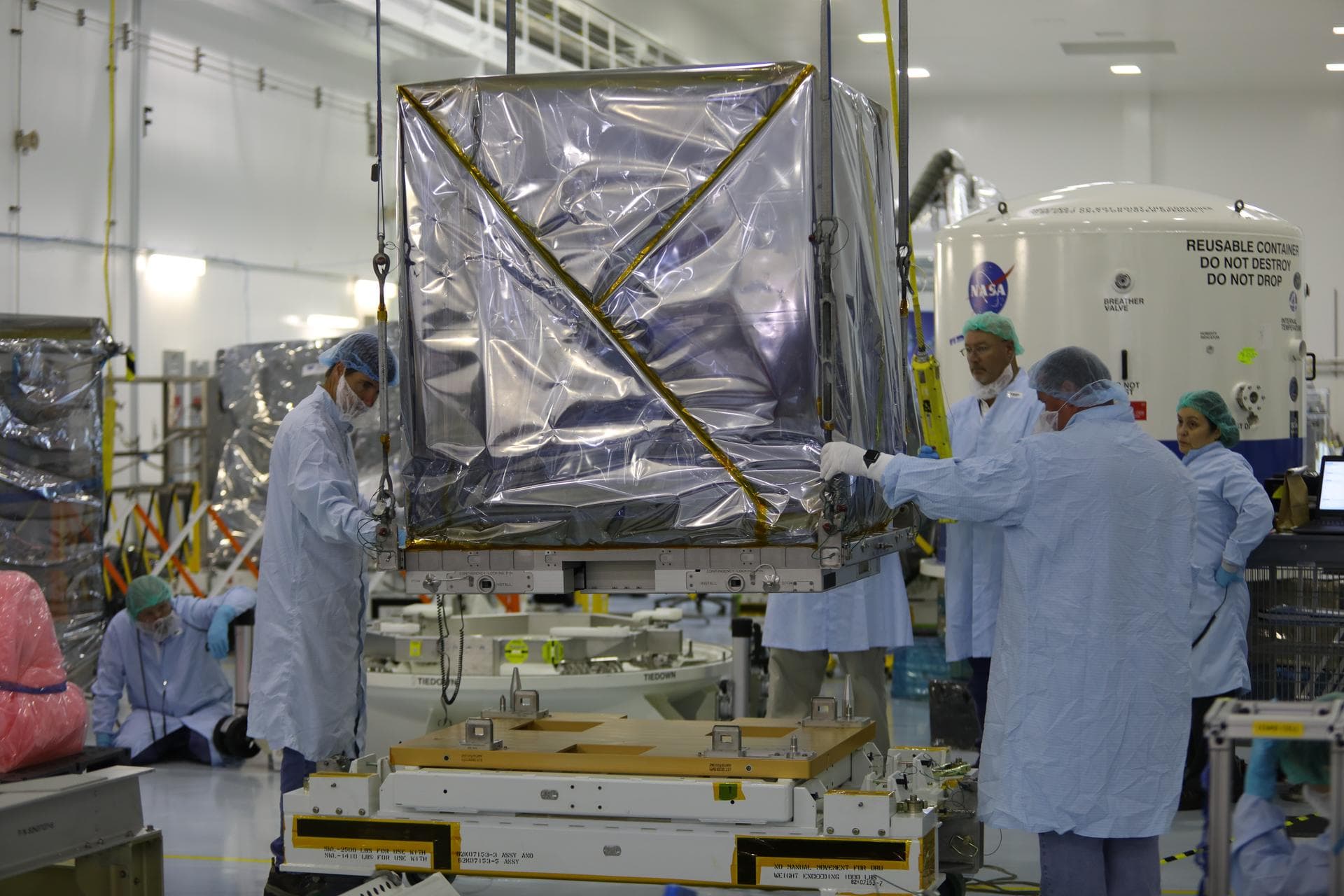 Inside the Space Station Processing Facility high bay at NASA's Kennedy Space Center in Florida, technicians assist as a crane is used to lift the Neutron star Interior Composition Explorer, or NICER,