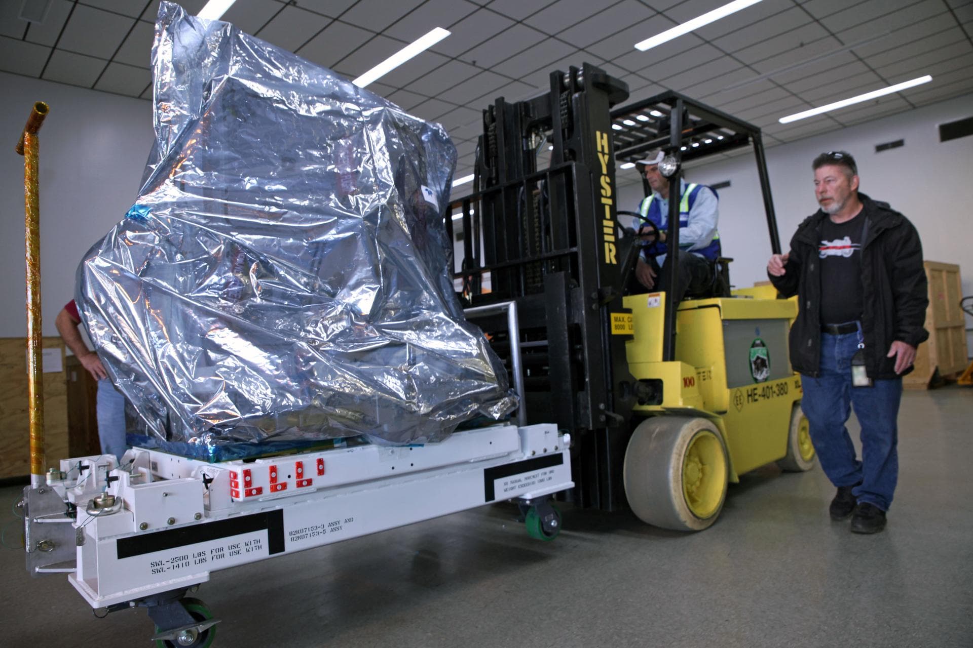 Technicians use a Hyster forklift to move the Multiple User System for Earth Sensing, or MUSES, payload out of the Space Station Processing Facility high bay at NASA's Kennedy Space Center in Florida.