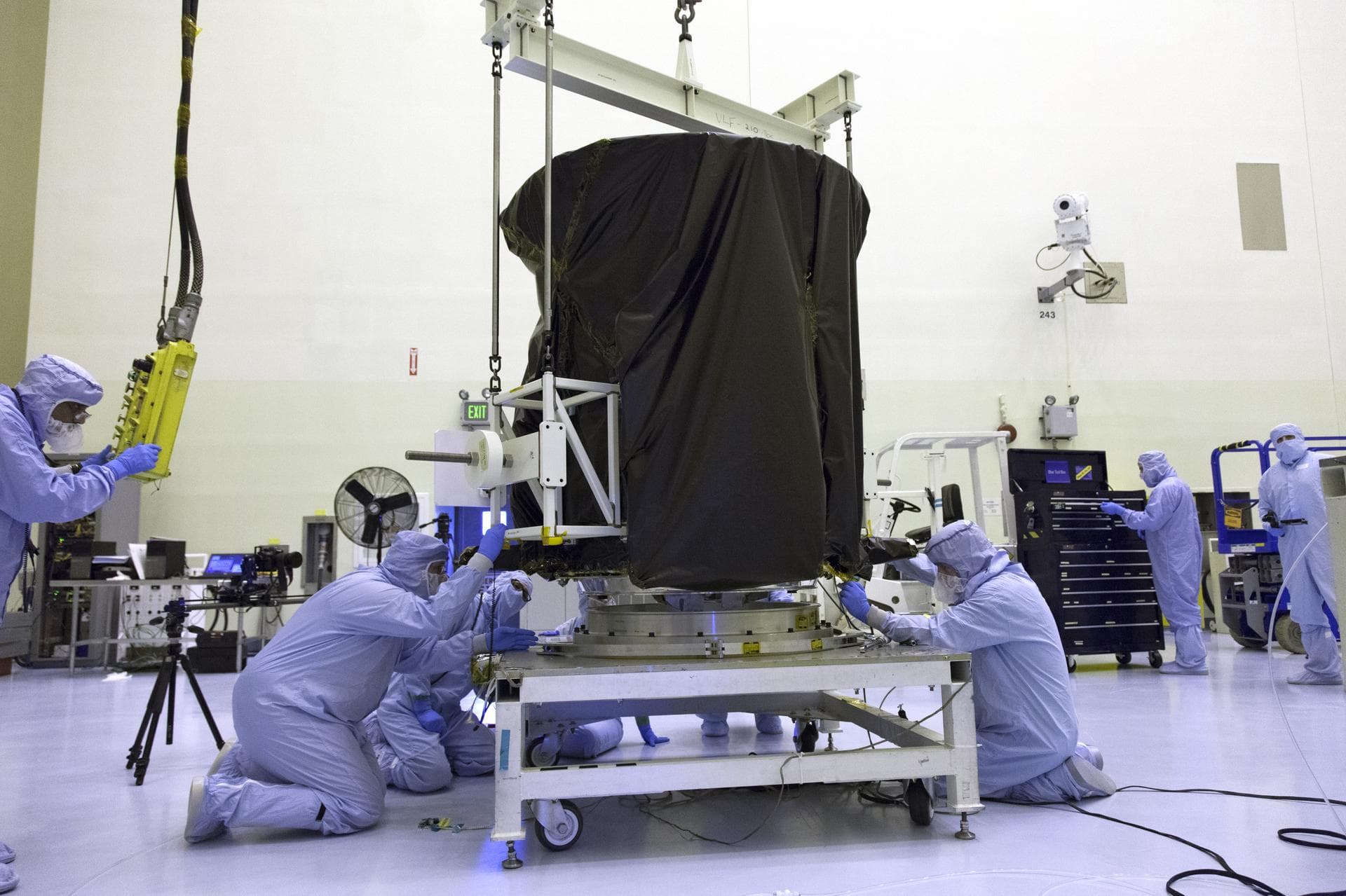 Technicians dressed in clean room suits monitor the progress as a crane lowers NASA's Transiting Exoplanet Survey Satellite (TESS) onto a test stand inside the Payload Hazardous Servicing Facility (PH