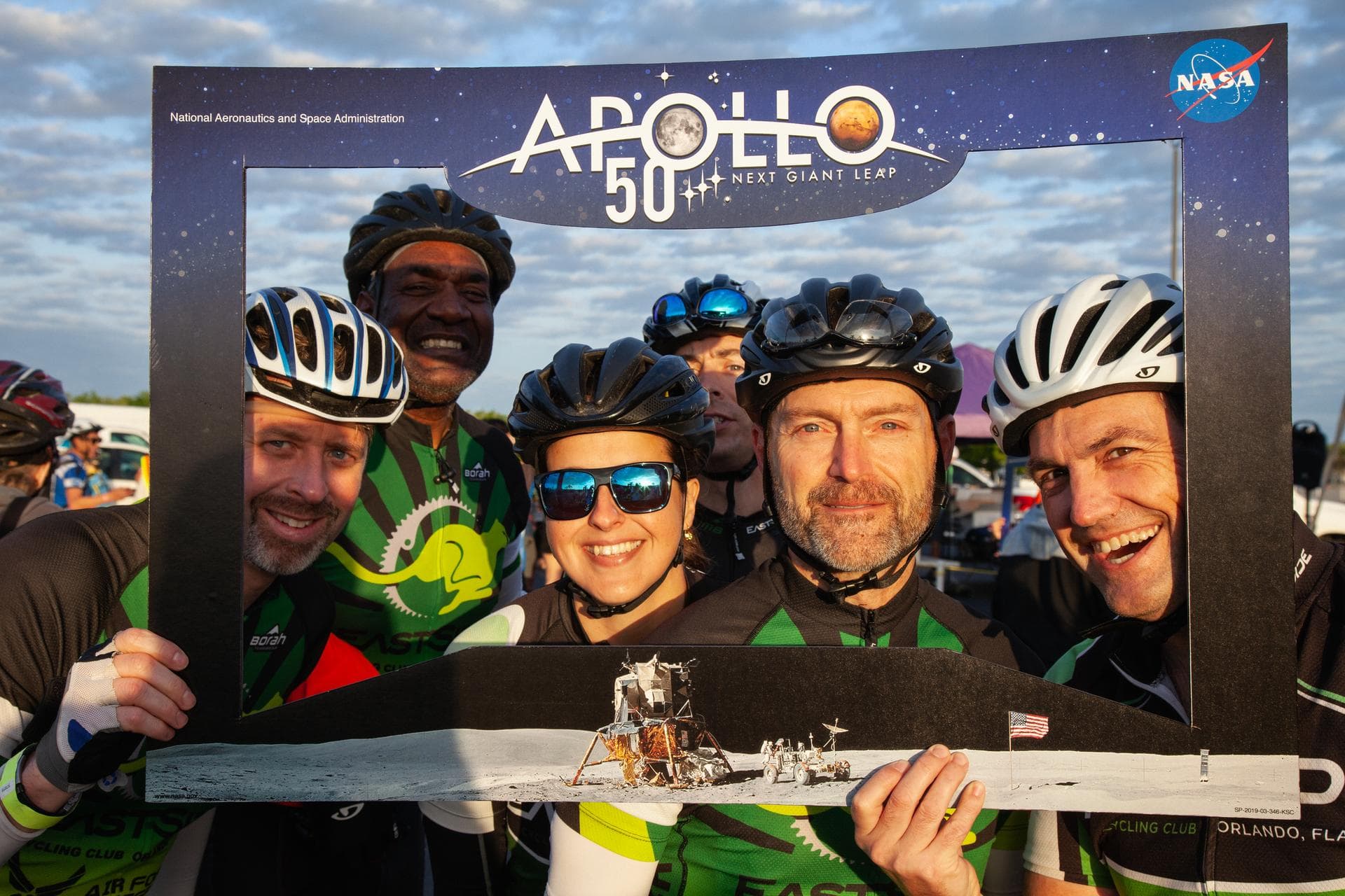 Cyclists pose for a photo within a frame promoting the 50th anniversary of the first Apollo Moon landing prior to the start of Kennedy Space Center’s annual Tour de KSC. The bicycle tour took place Ma