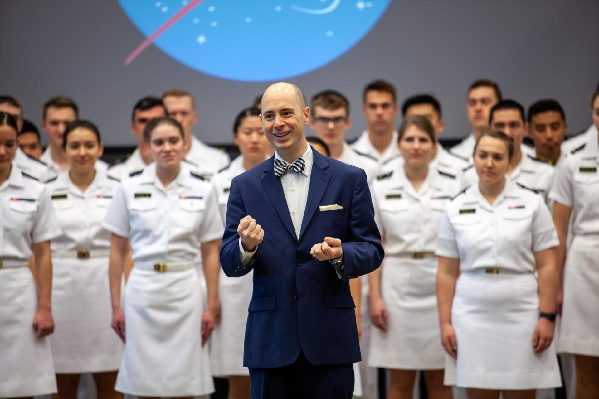 Dr. Aaron Smith, director and chairman, Musical Activities Department, United States Naval Academy, stands in front of the U.S. Naval Academy Glee Club during a performance for Kennedy Space Center em