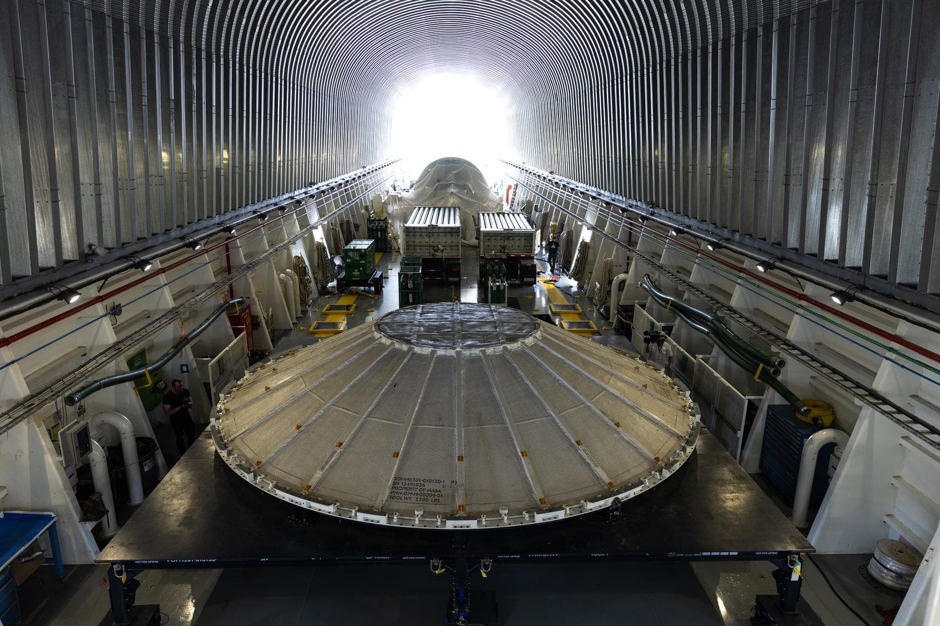 NASA’s Pegasus barge carrying the agency’s Nancy Grace Roman Space Telescope seen in the background of this photograph, and a weather cover for the Artemis III SLS (Space Launch System) rocket core st