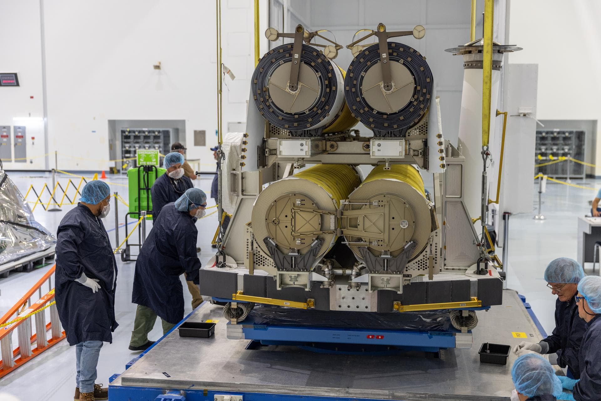 Technicians assist a crane to lower a pair of International Space Station Roll Out Solar Arrays (iROSA) onto a platform on Tuesday, Aug. 11, 2026, inside the Space Systems Processing Facility at NASA’