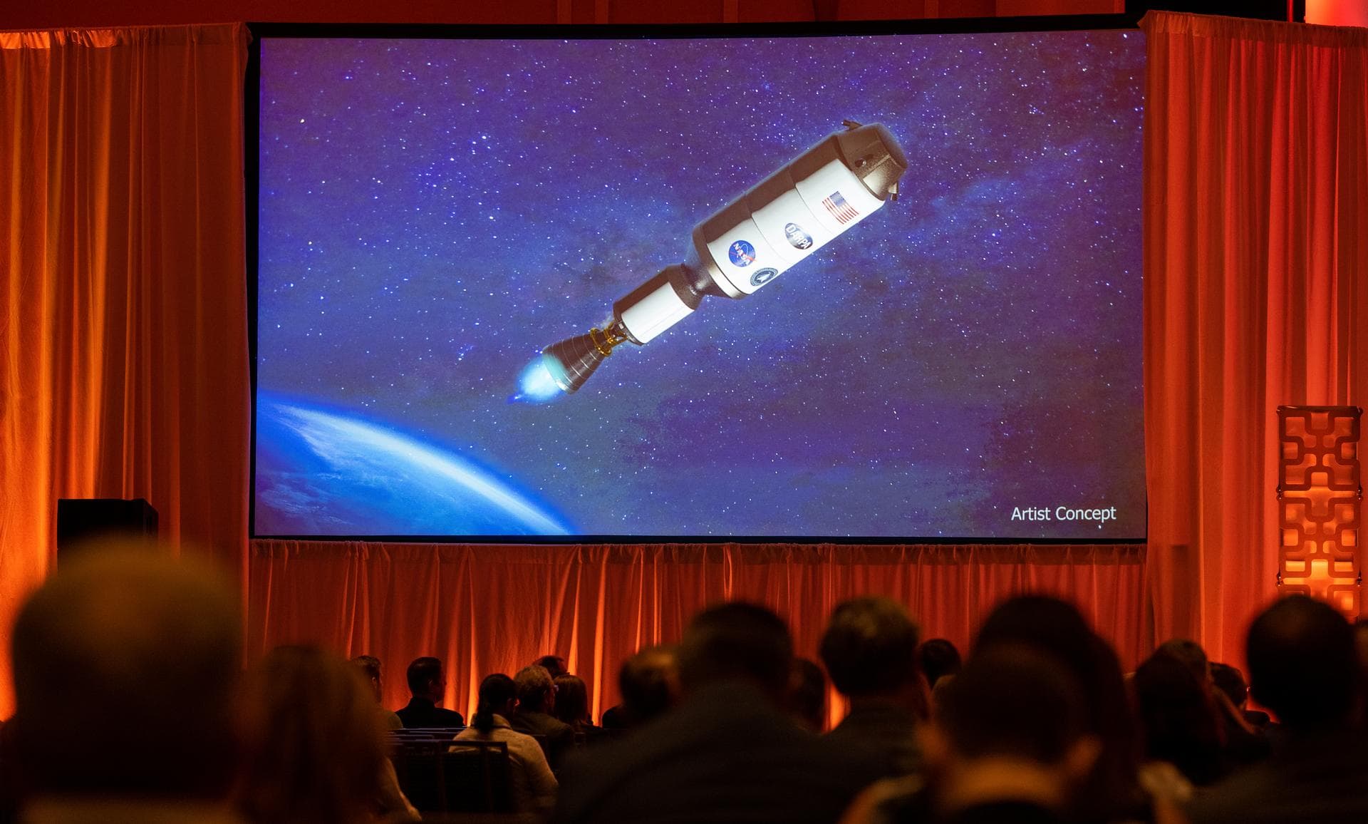 An artists concept of the Demonstration Rocket for Agile Cislunar Operations, or DRACO, spacecraft is seen on a screen during a fireside chat announcing a new collaboration on nuclear thermal propulsi
