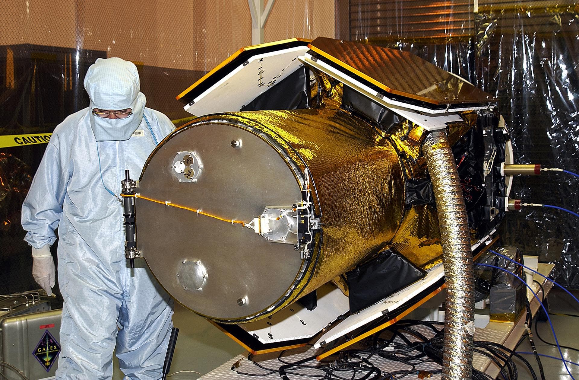 In the Multi-Payload Processing Facility, workers check the deployment of the cover of the telescope on NASA Galaxy Evolution Explorer, an orbiting space telescope observing galaxies in ultraviolet li