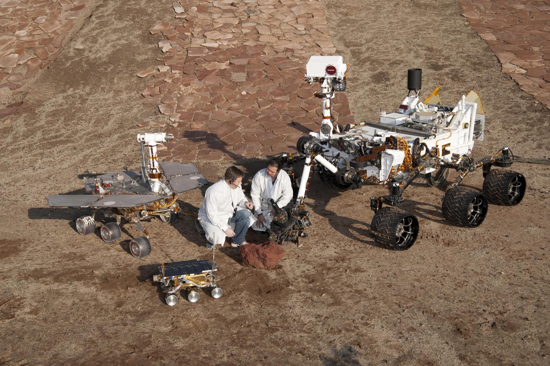 Two spacecraft engineers stand with three generations of Mars rovers developed at NASA JPL, Pasadena, Ca. Front and center is a flight spare of Sojourner, left is a working sibling to Spirit and Oppor