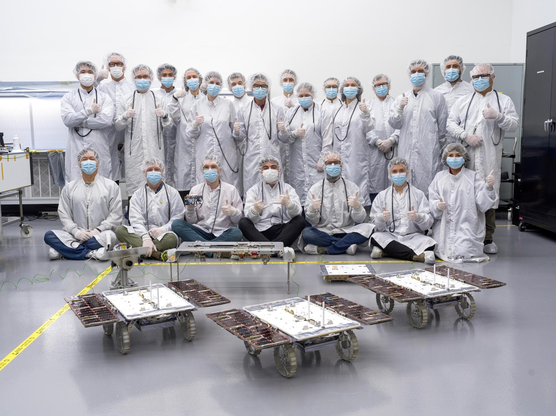 Members of the assembly, test, launch, and operations team for NASA's CADRE (Cooperative Autonomous Distributed Robotic Exploration) project pose in a clean room at the agency's Jet Propulsion Laborat