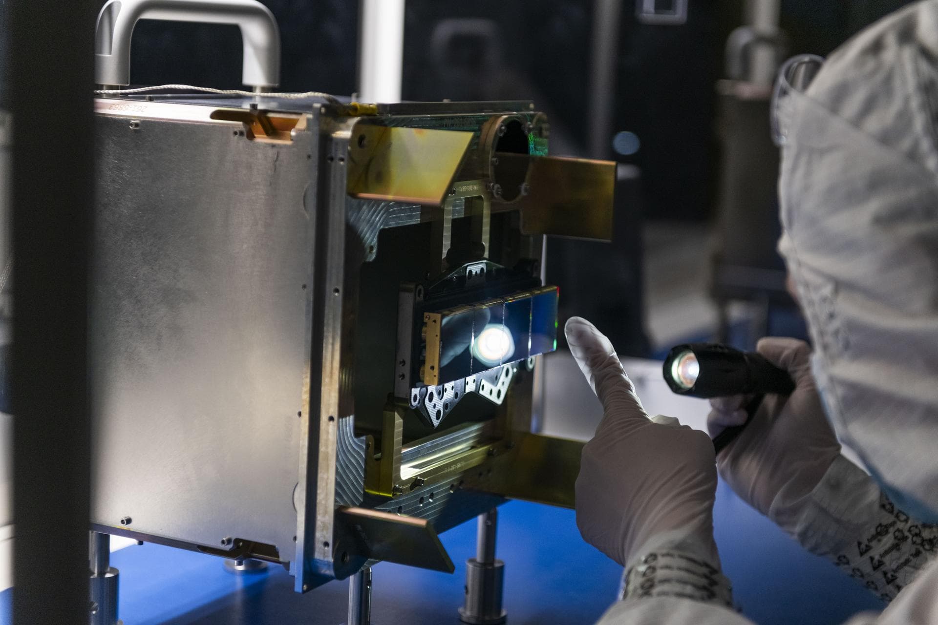 An engineer inspects the surface of four mid-wavelength infrared science detectors for NASA’s Near-Earth Object (NEO) Surveyor mission atop a clean room bench at the Space Dynamics Laboratory (SDL) in
