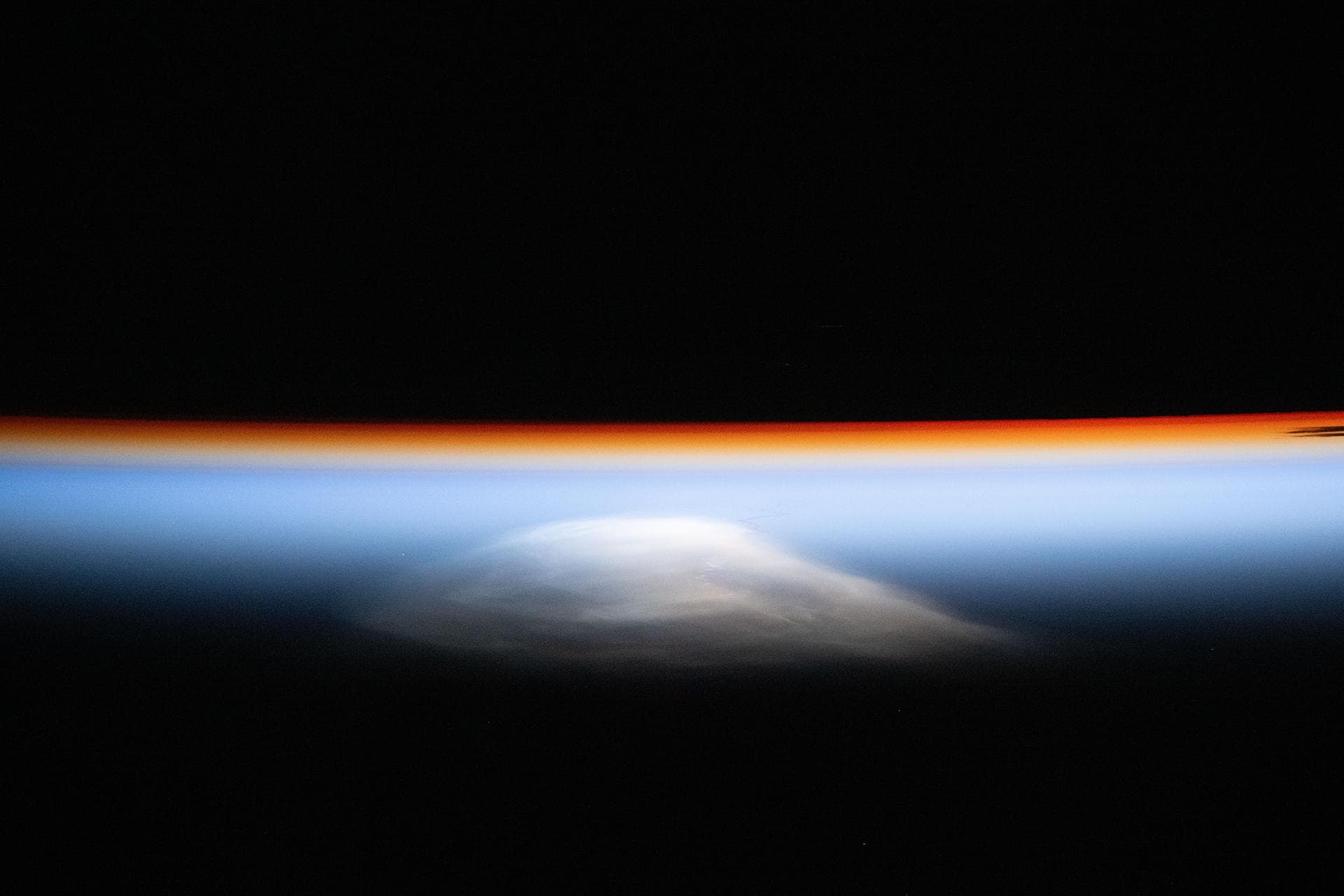 iss072e757530 (March 6, 2025) --- The last rays of an orbital sunset outline Earth’s horizon as a thin orange layer fades into blue, illuminating the atmosphere before nightfall. The wispy white featu